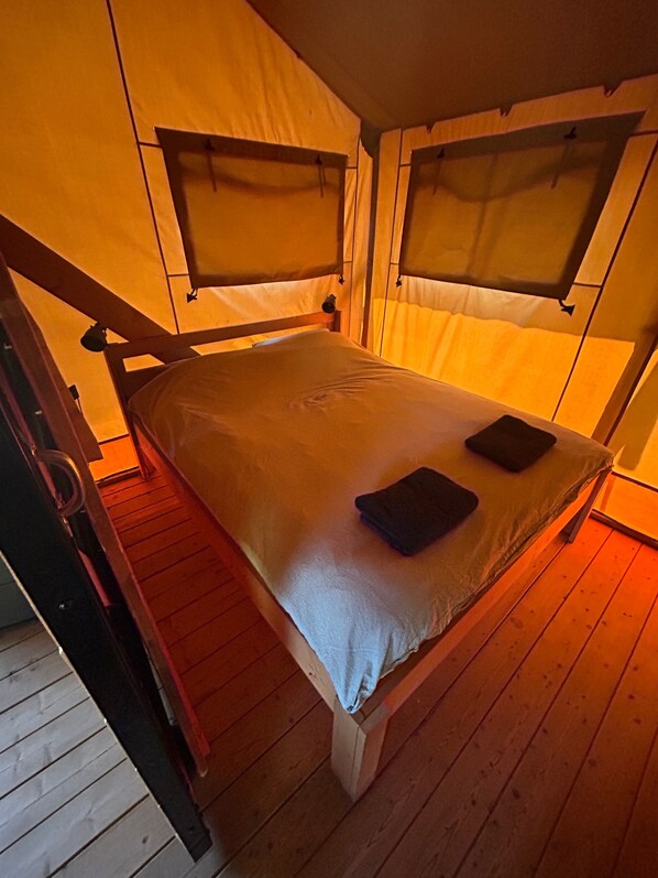 A single bed with a headboard and footboard, a wooden floor, and a window with a curtain.