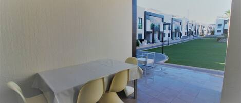 A modern dining area with a table and chairs, a view of a well-maintained lawn and buildings in the background.