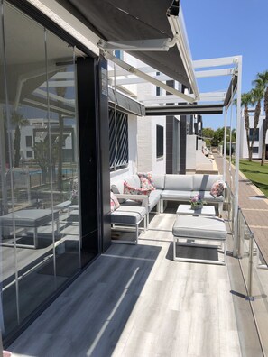 Eine moderne Außenpatio mit Glasveranda, einer grauen Sofagarnitur und einem Pool im Hintergrund.