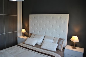 A bedroom with a tufted headboard, two bedside tables with lamps, and a bed with a striped bedspread. - Groundfloor Oasis Beach II La Zenia (Orihuela)