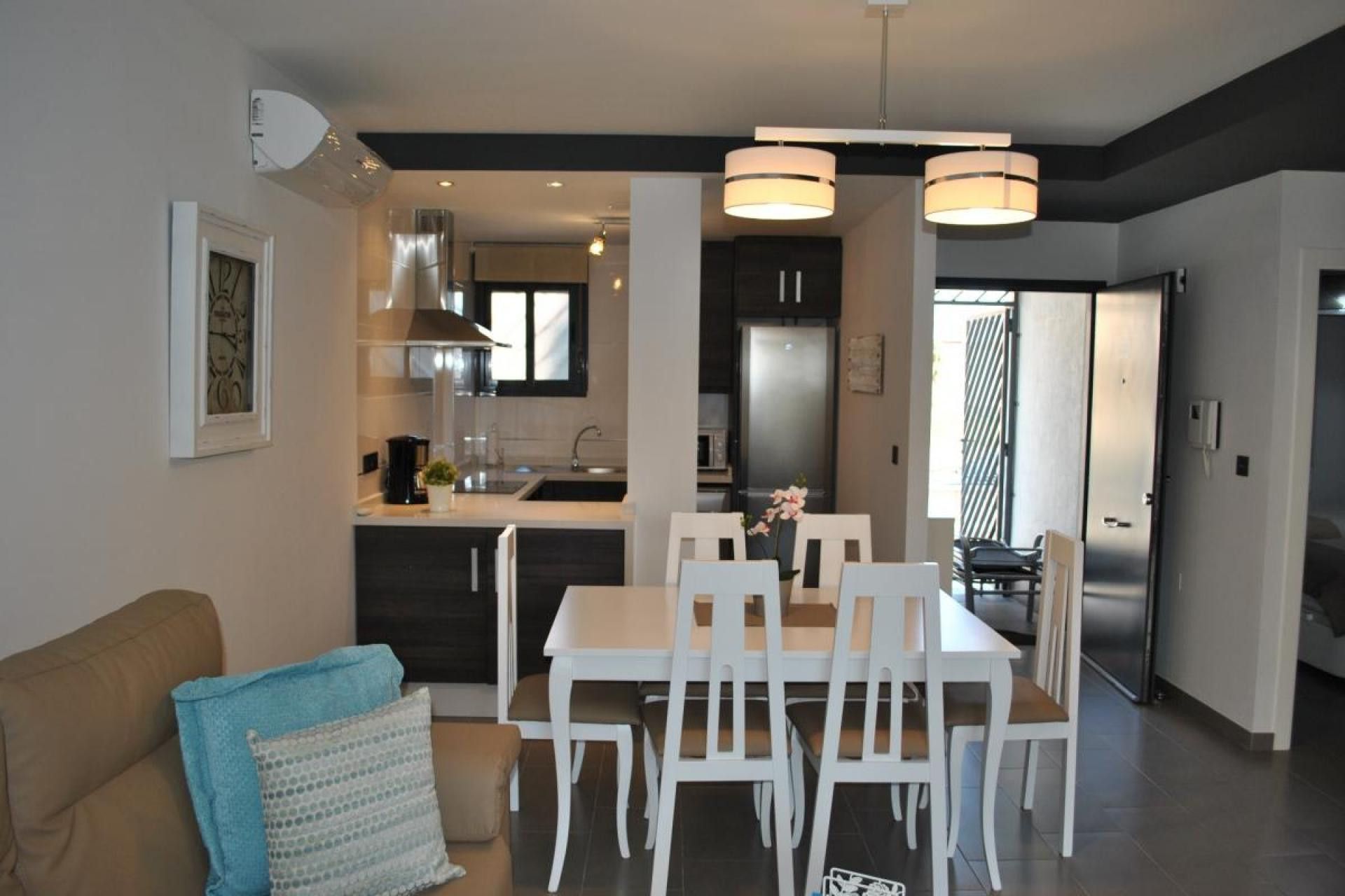A modern kitchen with a dining area, featuring a central island, white chairs, and pendant lighting.