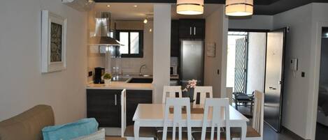 A modern kitchen with a dining area, featuring a central island, white chairs, and pendant lighting.