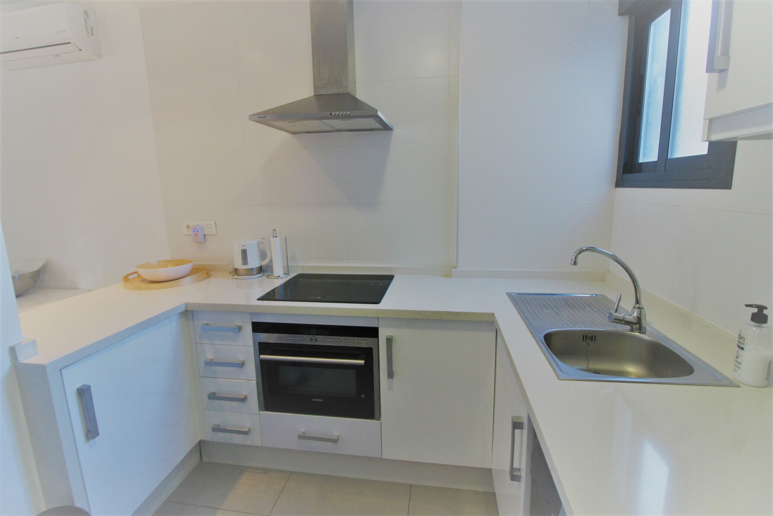 A compact kitchen with white cabinetry, a built-in oven, a stainless steel sink, and a window above the sink.