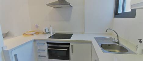 A compact kitchen with white cabinetry, a built-in oven, a stainless steel sink, and a window above the sink.