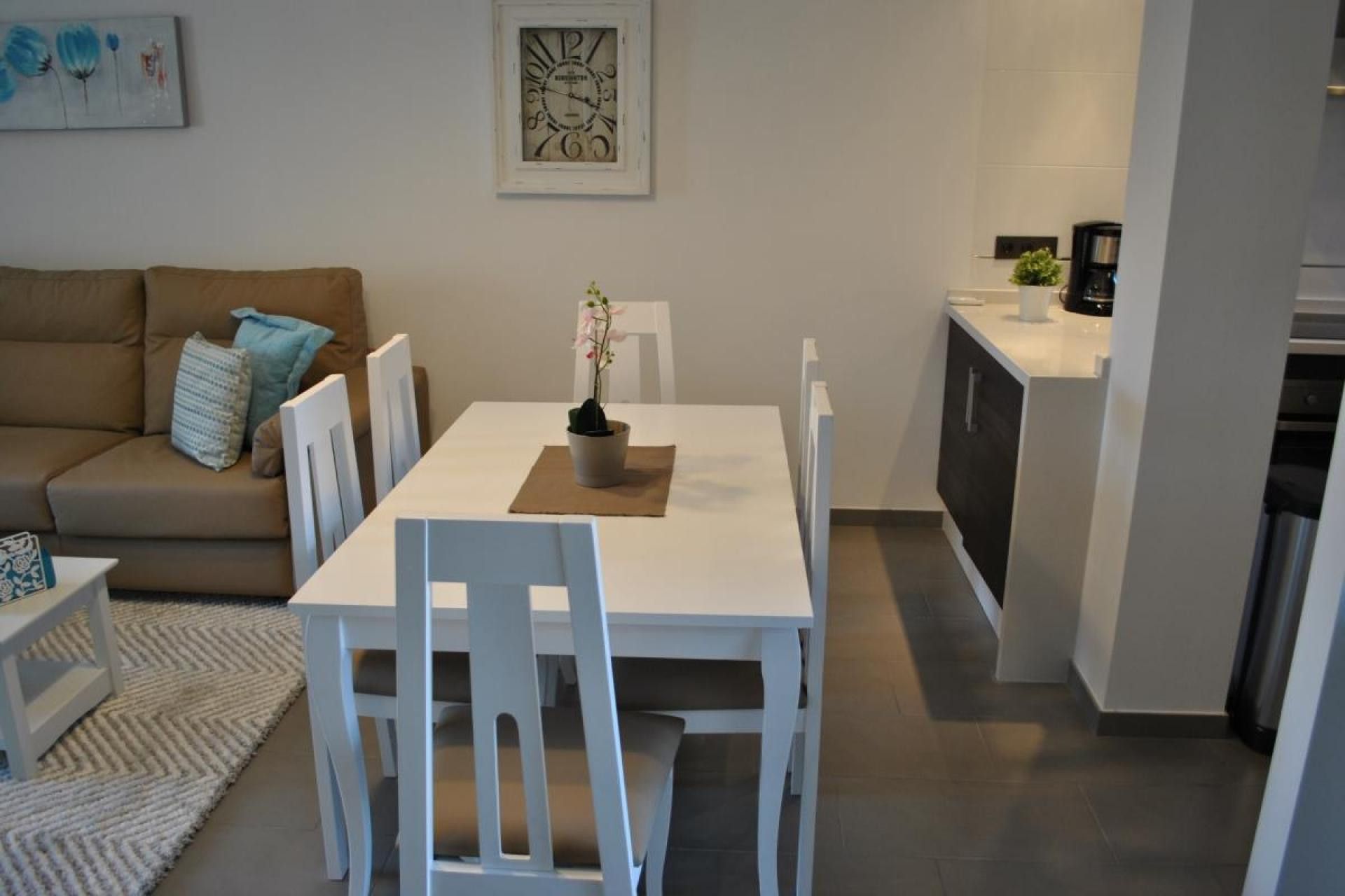Un espace de vie compact comprenant une table et des chaises, un canapé, un petit coin cuisine et une horloge encadrée accrochée au mur.