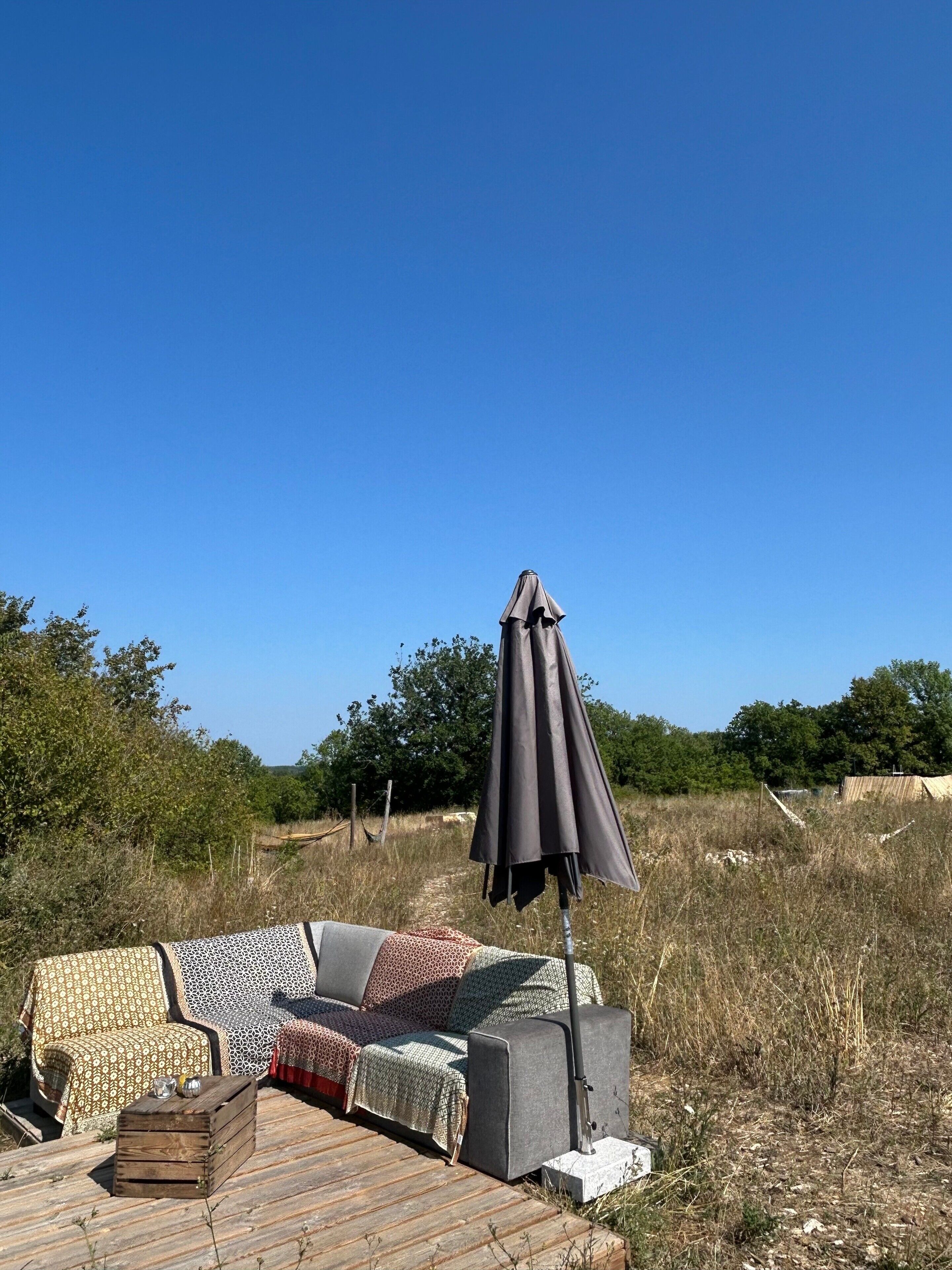 An outdoor seating area with a sofa and a table, an umbrella, and a view of the surrounding landscape.