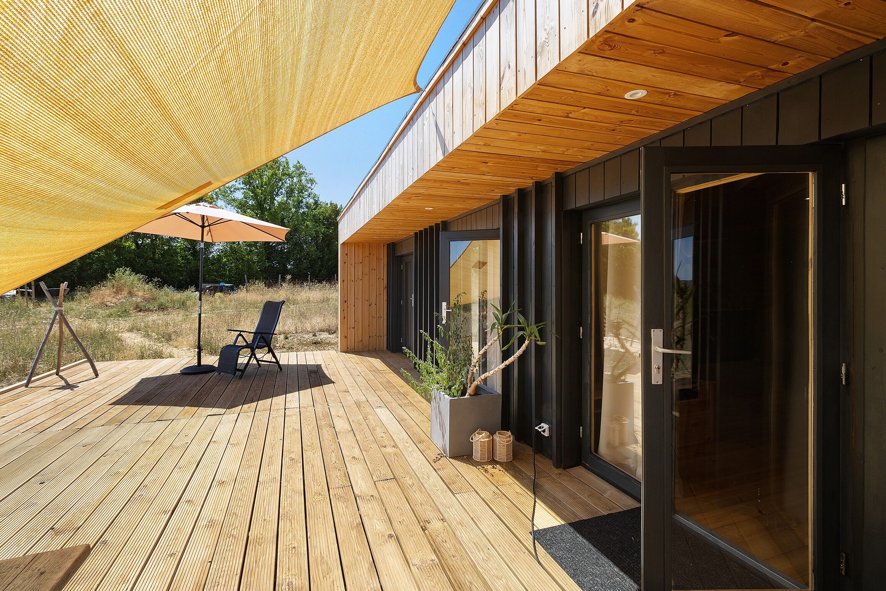 Eine Holzterrasse mit Sitzgelegenheit und einem großen Sonnenschirm.