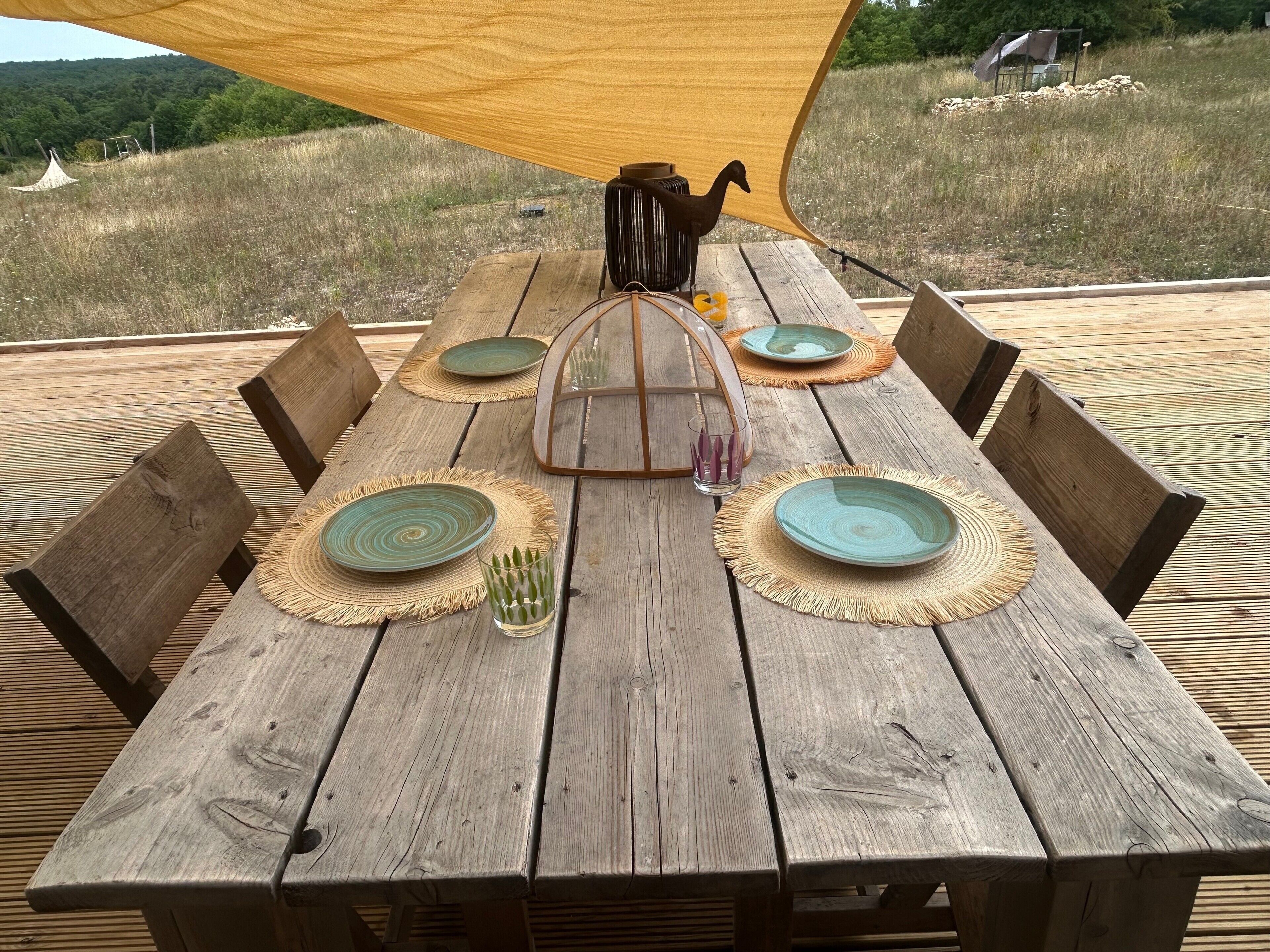 A wooden dining table with woven placemats, plates, and a glass.