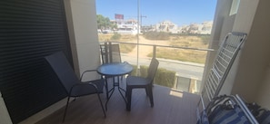 A balcony with a table and chairs, a view of a road and buildings, and a metal railing. - Apartment Zenia Beach La Zenia (Orihuela)