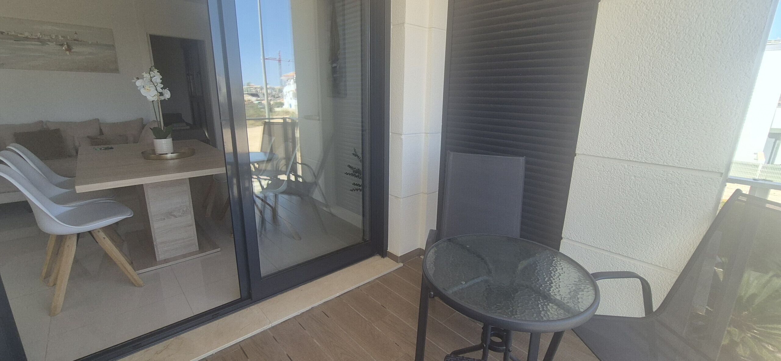 A balcony with a glass door, a dining table with chairs, and a small table with a chair.