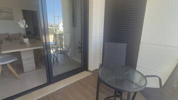 A balcony with a glass door, a dining table with chairs, and a small table with a chair.