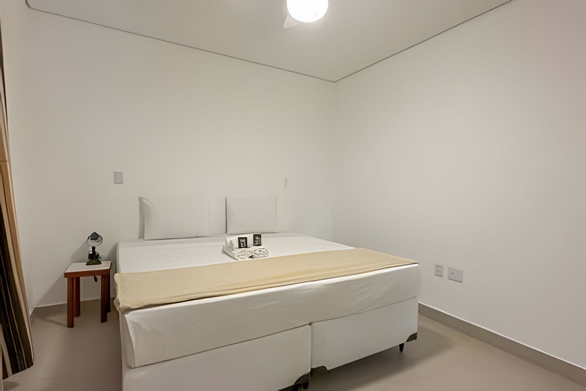 Ein Schlafzimmer mit Bett, Nachttisch, Lampe und einem kleinen Hocker.