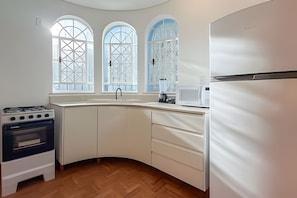 Cocina con estufa, microondas y refrigerador, amplias ventanas arqueadas y piso de madera.