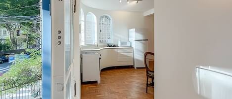Una cocina moderna con muebles blancos, piso de madera en patrón de espiga y vista a la ciudad a través de amplios ventanales.