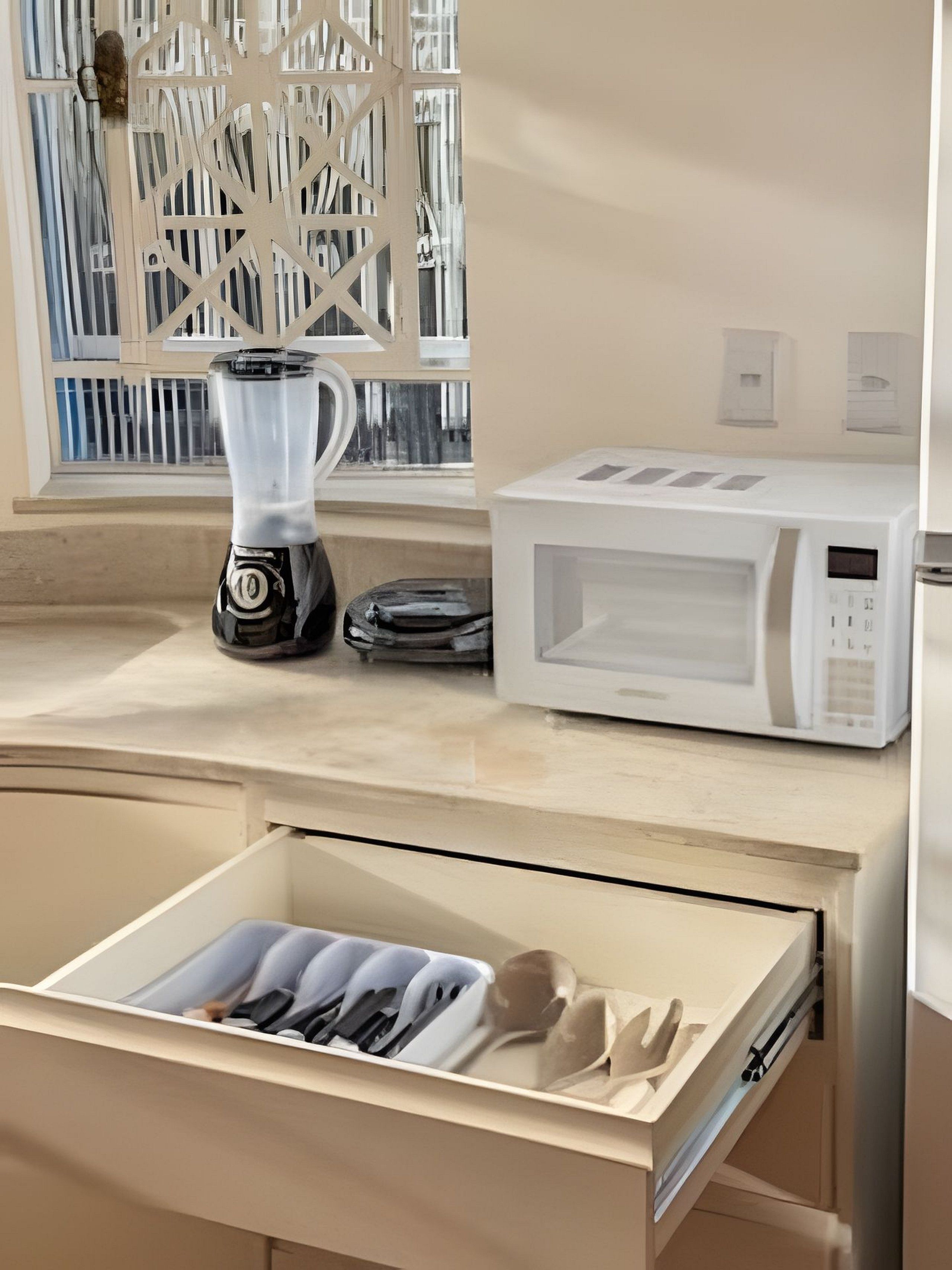 A kitchen with a coffee maker, microwave, and a drawer with utensils.