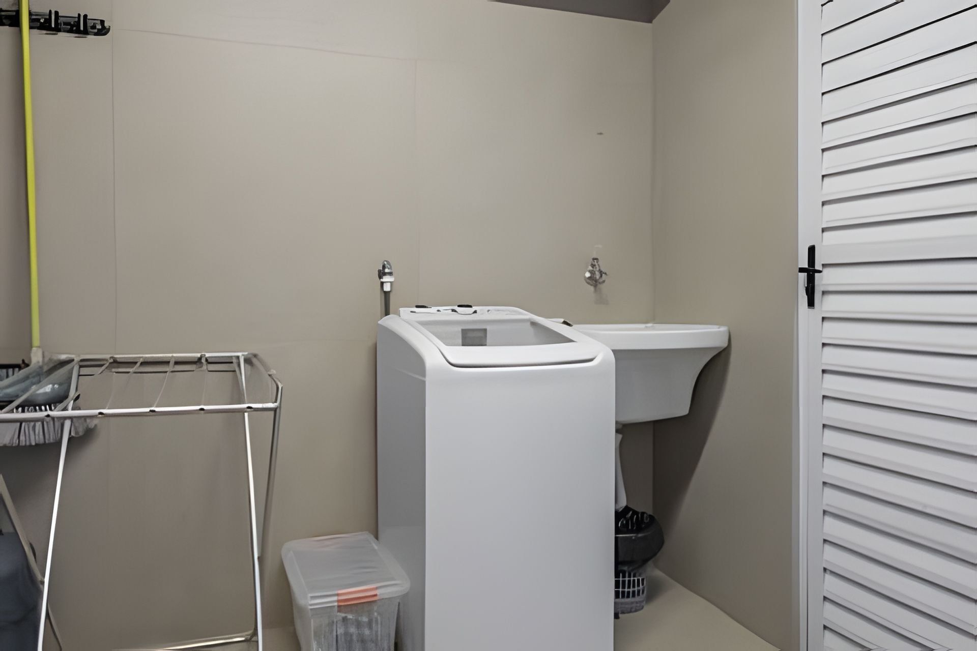 A laundry room with a washing machine, a sink, and a drying rack.
