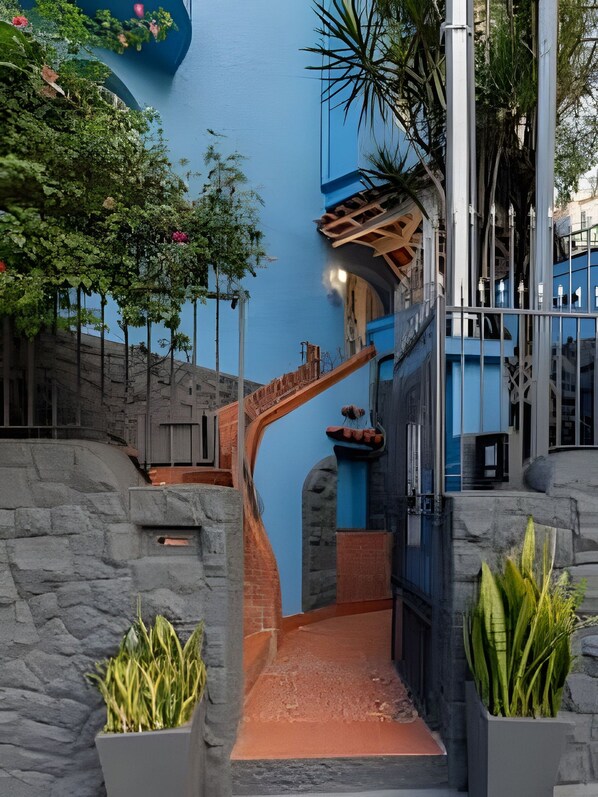 Una escalera con pared azul, muros de piedra y plantas en macetas.