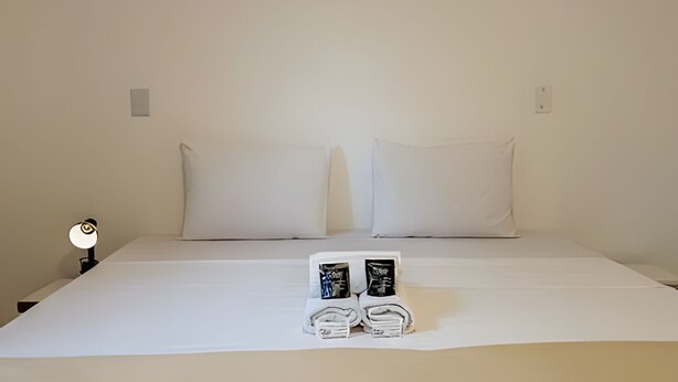 A bed with white linens, two pillows, and a pair of towels with a small photo on them.