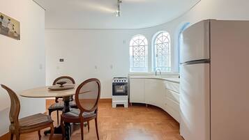 A compact kitchen with a round dining table, wooden chairs, a built-in oven, and a refrigerator.