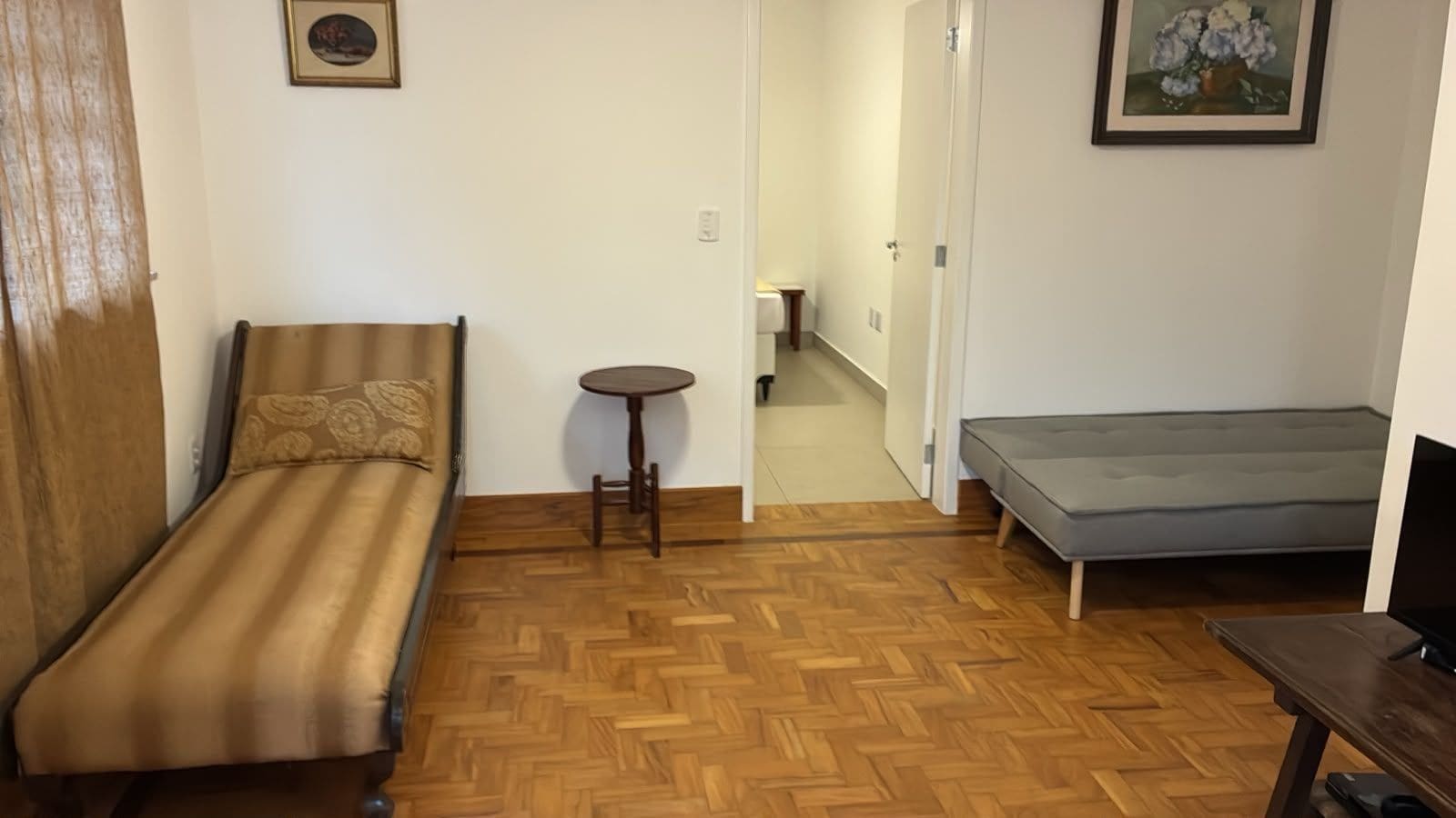 A room with a single bed, a small round table, a sofa, and a door leading to a hallway.