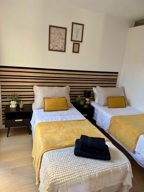 A hotel room with two beds, each with a white bedspread and a yellow throw blanket. There are two bedside tables with decorative items and a wall-mounted headboard. - Groundfloor Zenia Beach La Zenia (Orihuela)