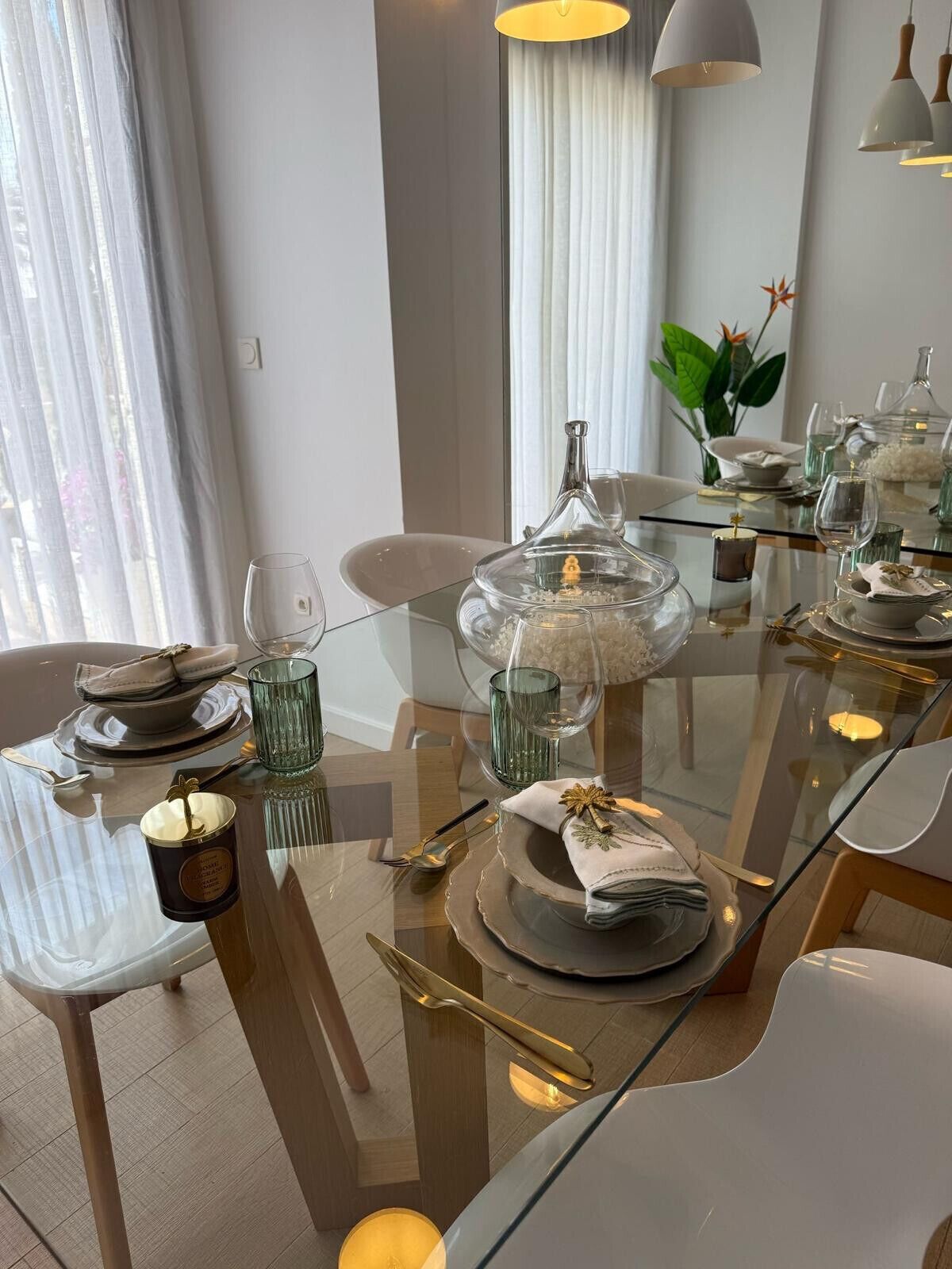 Un espace repas moderne avec une table en verre dressée pour un repas, agrémentée de beaux verres transparents, d’un centre de table décoratif et d’une élégante vaisselle.