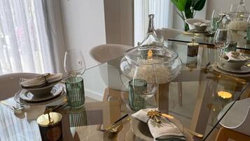 Un espace repas moderne avec une table en verre dressée pour un repas, agrémentée de beaux verres transparents, d’un centre de table décoratif et d’une élégante vaisselle.