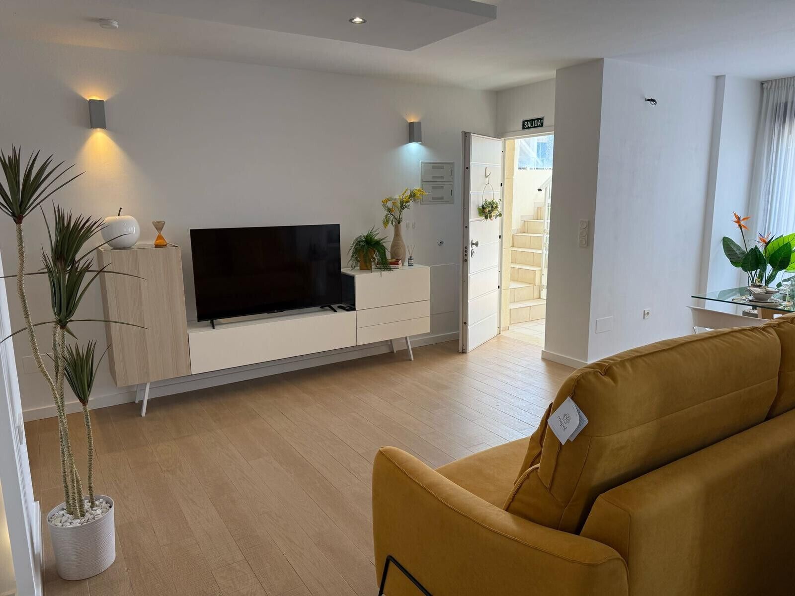 Ein modernes Wohnzimmer mit Flachbildfernseher, einer Couch und einem Essbereich mit Glastisch.