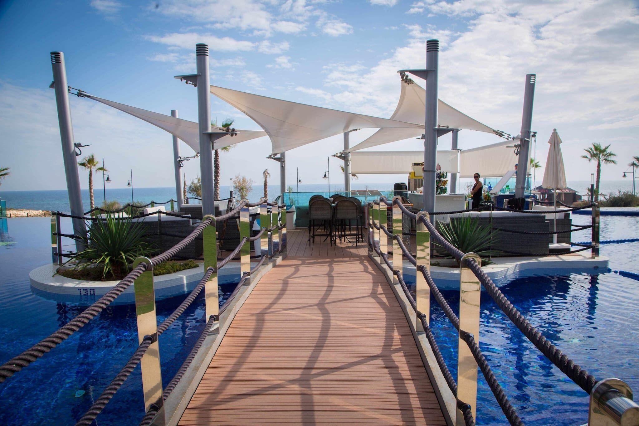 Eine Holzterrasse führt zu einem Poolbereich mit Liegestühlen und Sonnenschirmen mit Blick aufs Meer.