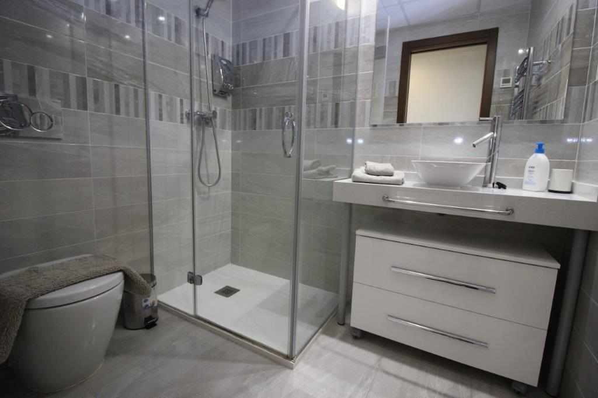 A modern bathroom with a glass-enclosed shower, a white sink, and a mirror above it.