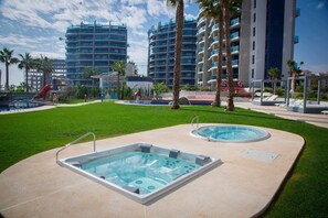 Ein Poolbereich mit zwei Whirlpools und einer Rutsche, umgeben von Palmen und modernen Gebäuden.