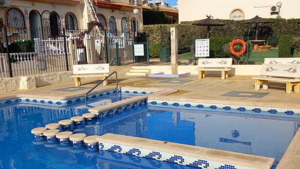 A swimming pool with steps leading into it, surrounded by a fence and a sign indicating a lifeguard on duty. - Groundfloor Spanish House La Florida (Orihuela)