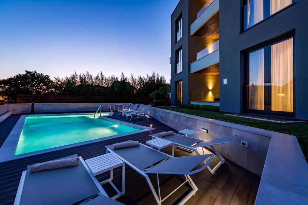 A modern building with a swimming pool, lounge chairs, and a well-lit outdoor area.