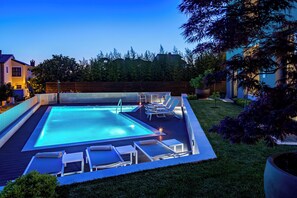 A rectangular swimming pool with a deck area, surrounded by a wooden fence and a grassy lawn.
