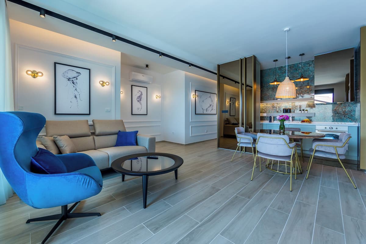 A modern living room with a blue armchair, a sofa, and a dining area with a table and chairs.