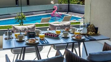 A breakfast setup with a table, chairs, and a pool with a flamingo float.