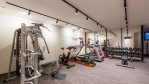 A modern gym with various exercise equipment, including cardio machines, free weights, and a mirrored wall. - Rocca Riviera  (Umag)