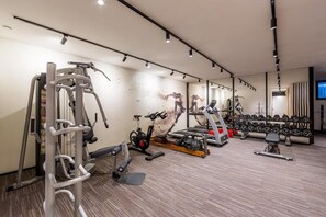 A modern gym with various exercise equipment, including cardio machines, free weights, and a mirrored wall.