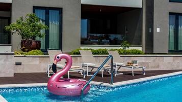 Ein Swimmingpool mit einem rosa Schwaneinhorn-Badeartikel, Liegestühlen und einem Blumentopf.