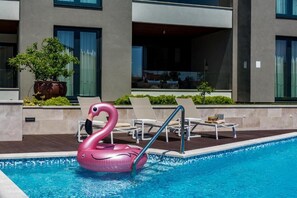 A swimming pool with a pink swan float, lounge chairs, and a potted plant.