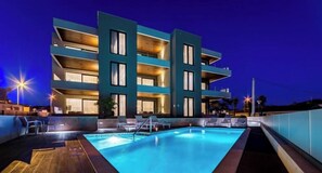 A modern hotel with a rooftop pool, multiple balconies, and outdoor seating.