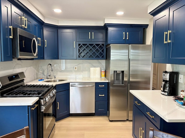 A modern kitchen with dark blue cabinets, stainless steel appliances, and a white countertop.