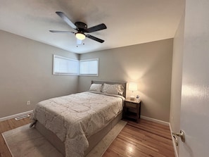 A bedroom with a bed, nightstand, lamp, ceiling fan, and windows.