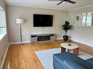A living room with a flat-screen TV mounted on the wall, a floor lamp, a potted plant, a coffee table, and a blue sofa.
