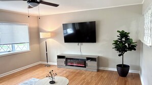 Un salon moderne doté d’un téléviseur à écran plat, d’un ventilateur de plafond, d’une lampe sur pied, d’une cheminée, d’une table basse ronde et d’une plante en pot.