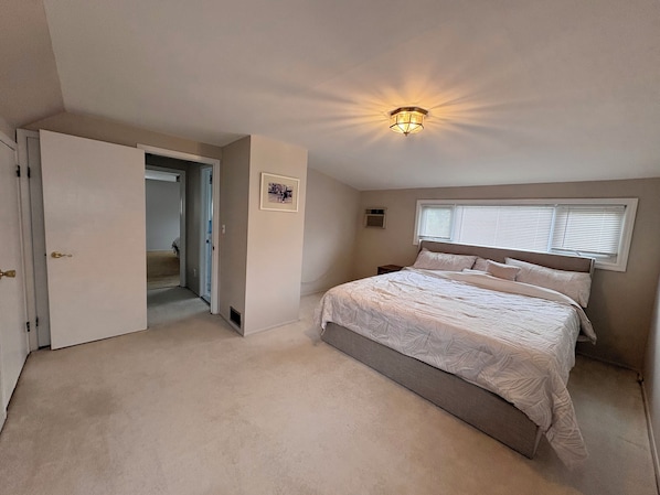 Un dormitorio con una cama grande, una lámpara de techo, una ventana con persianas y una puerta que da a otra habitación.
