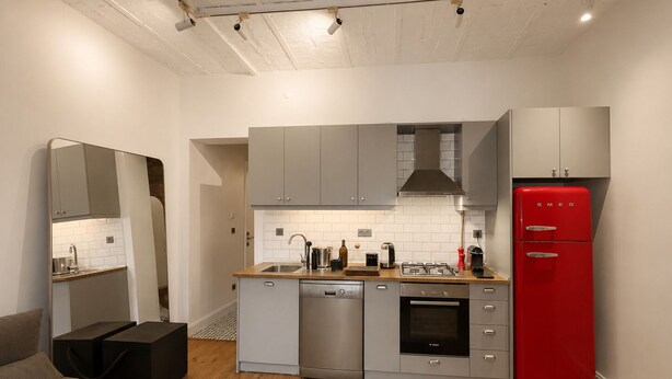 Une cuisine de taille réduite avec des meubles gris, un réfrigérateur rouge, un lave-vaisselle et une cuisinière.