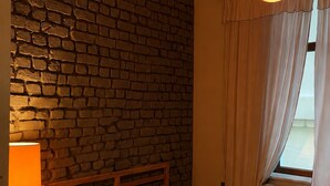 Une pièce avec un mur en briques, un lit, une lampe et une fenêtre avec des rideaux.