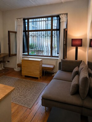 Ein Wohnzimmer mit einer Couch, einem Holzschrank, einem kleinen Tisch und einem Fenster mit Vorhängen.