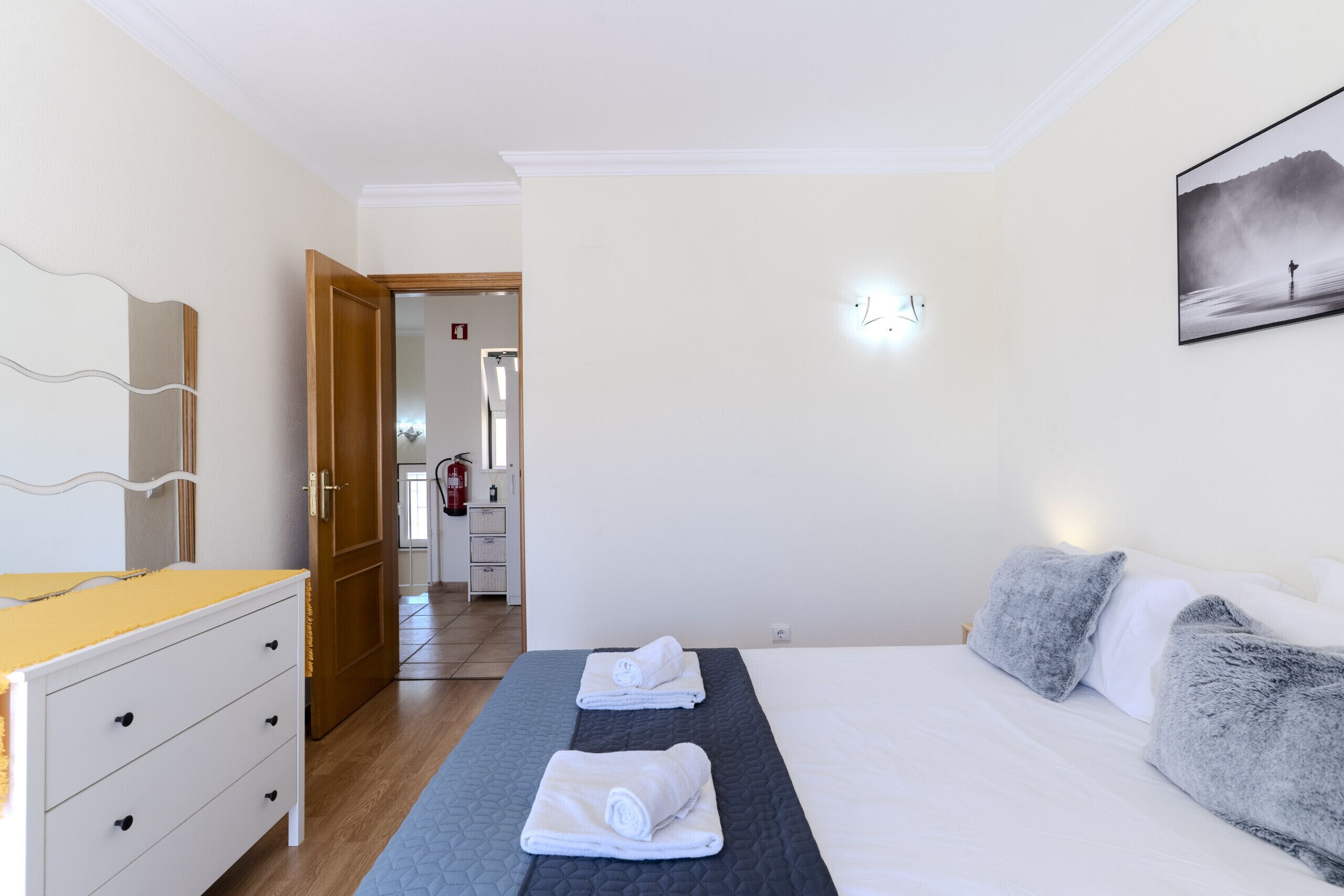 Una habitación de hotel con cama, mesita de noche, espejo y puerta que da a un baño.